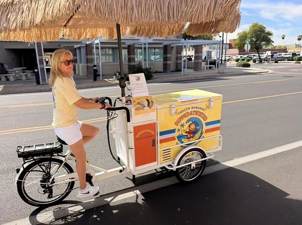 Jules riding the Dipped and Twisted e-trike cart under its tiki umbrella
